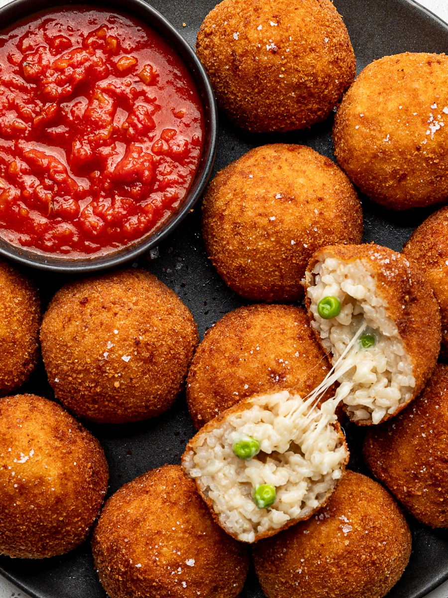 Close up of arancini balls with one arancini cut open and showing the cheesy inside.