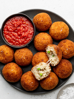 Fried arancini balls on a black plate with a bowl of marinara sauce on the side.