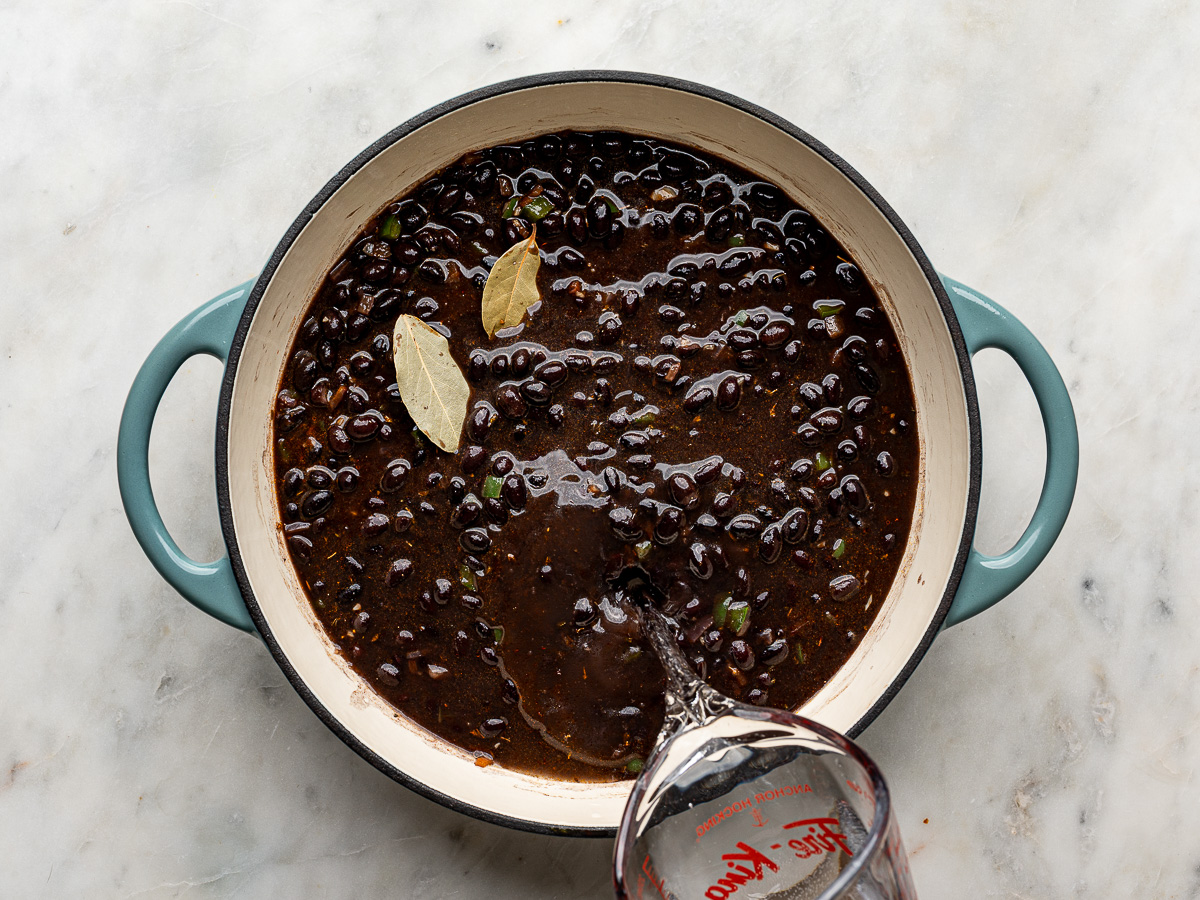Adding water to a skillet of black beans and their liquid while cooking with spices.