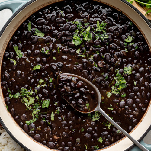Creamy cooked canned black beans in a green skillet garnished with fresh cilantro.