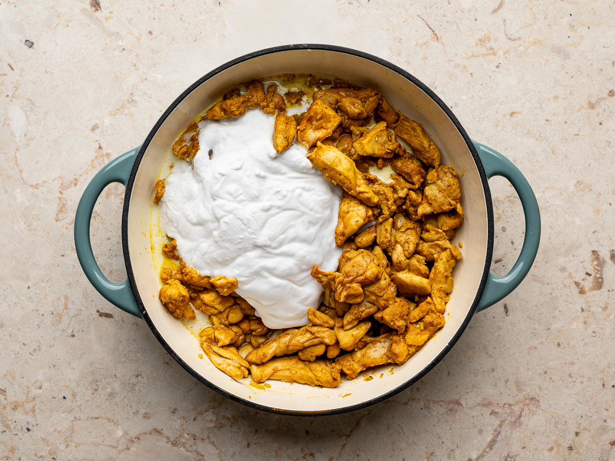 Chicken simmering in a pan as chicken broth and coconut milk are poured in, creating a rich curry sauce.