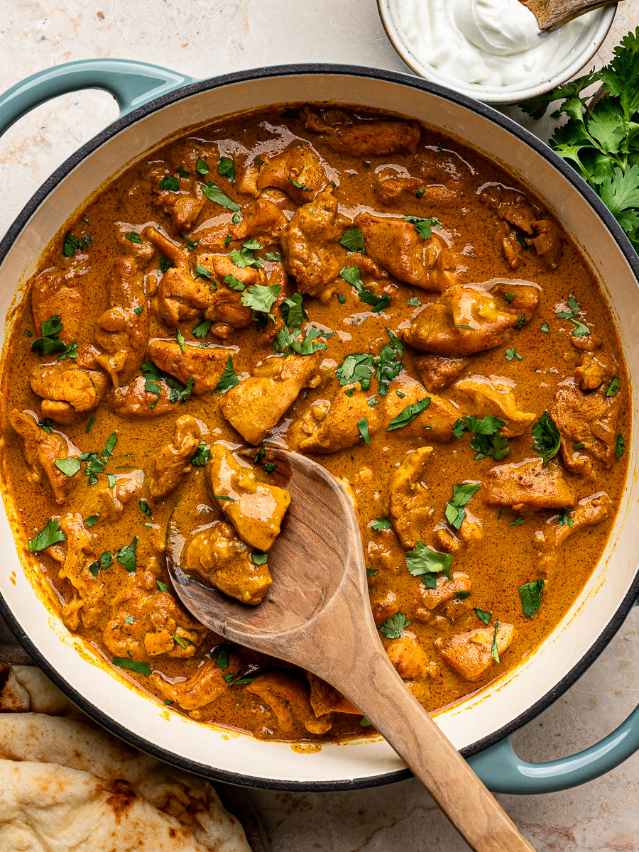 Finished coconut chicken curry in a pan, topped with fresh cilantro, with naan and a dollop of yogurt served alongside.