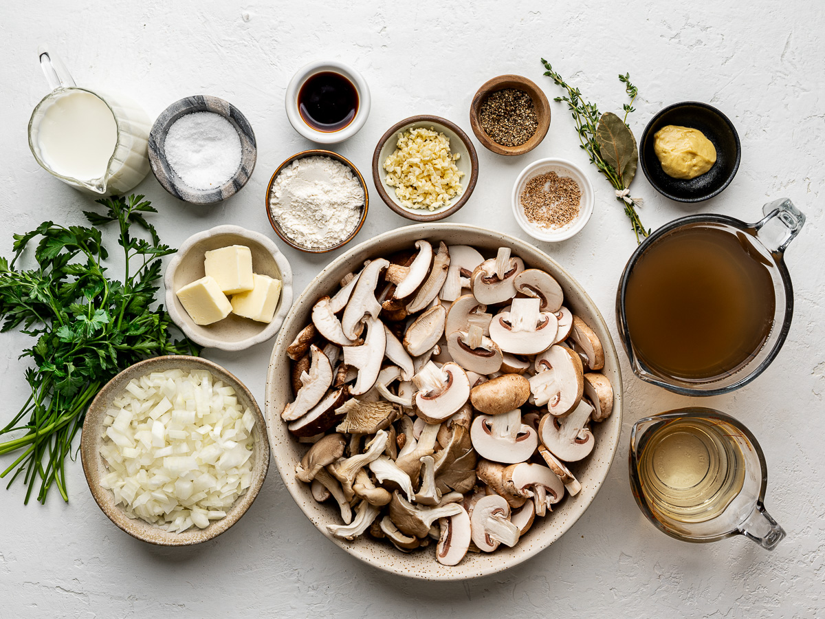 Ingredients for creamy mushroom soup arranged in small bowls, including mushrooms, onion, garlic, herbs, broth, milk, and soy sauce.
