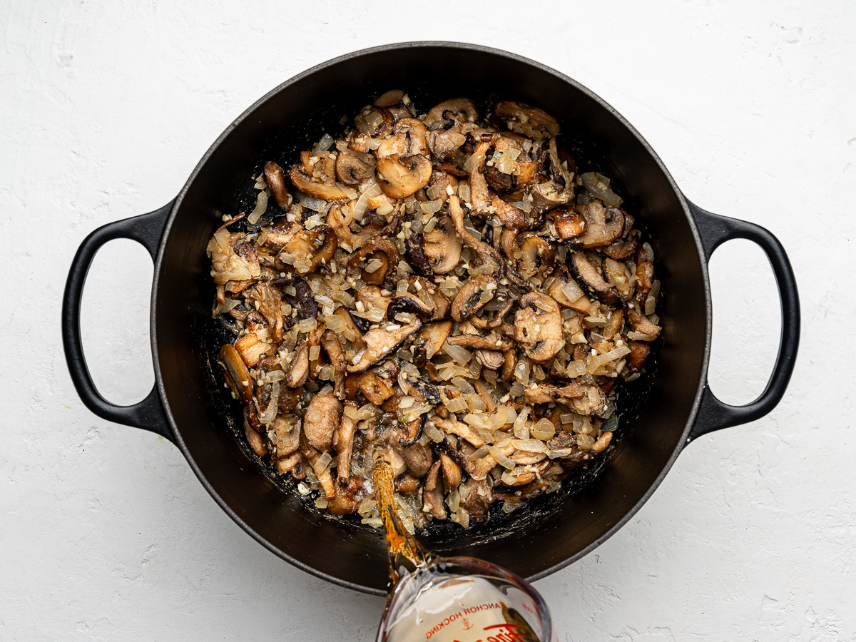 White wine being poured into a pot of sautéed mushrooms to deglaze.