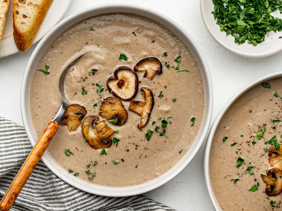 Creamy mushroom soup served in two white bowls garnished with sliced mushrooms and chopped parsley.