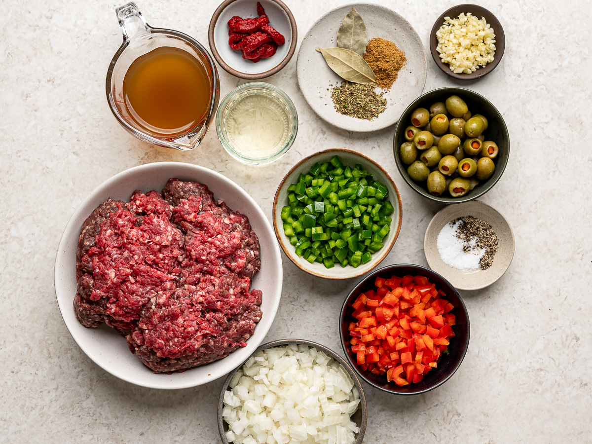 Ingredeints for empanada beef filling (ground beef, onions, bell peppers, garlic, spices, tomato paste and broth) prepared in individual bowls.
