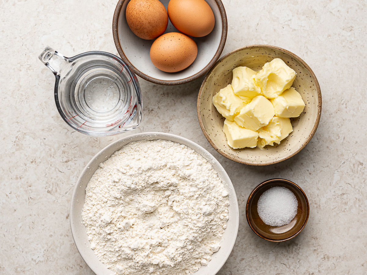 Ingredients for empanada dough (water, flour, butter, and salt) prepared in individual bowls.