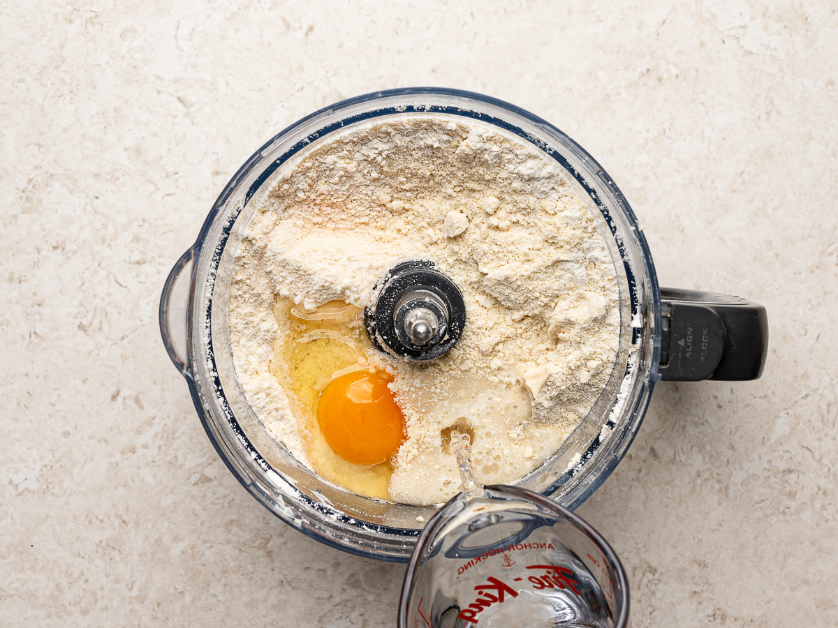 Adding water to flour and egg in food processor to make empanada dough.