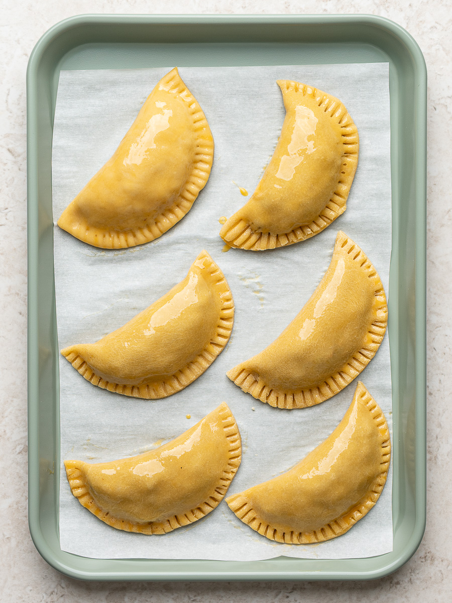 Unbaked empanadas on baking sheet with fork crimp seal.