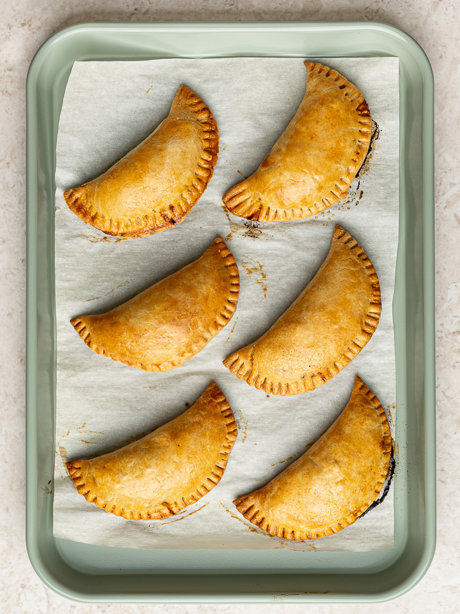 Baked empanadas on baking sheet with fork crimp seal.