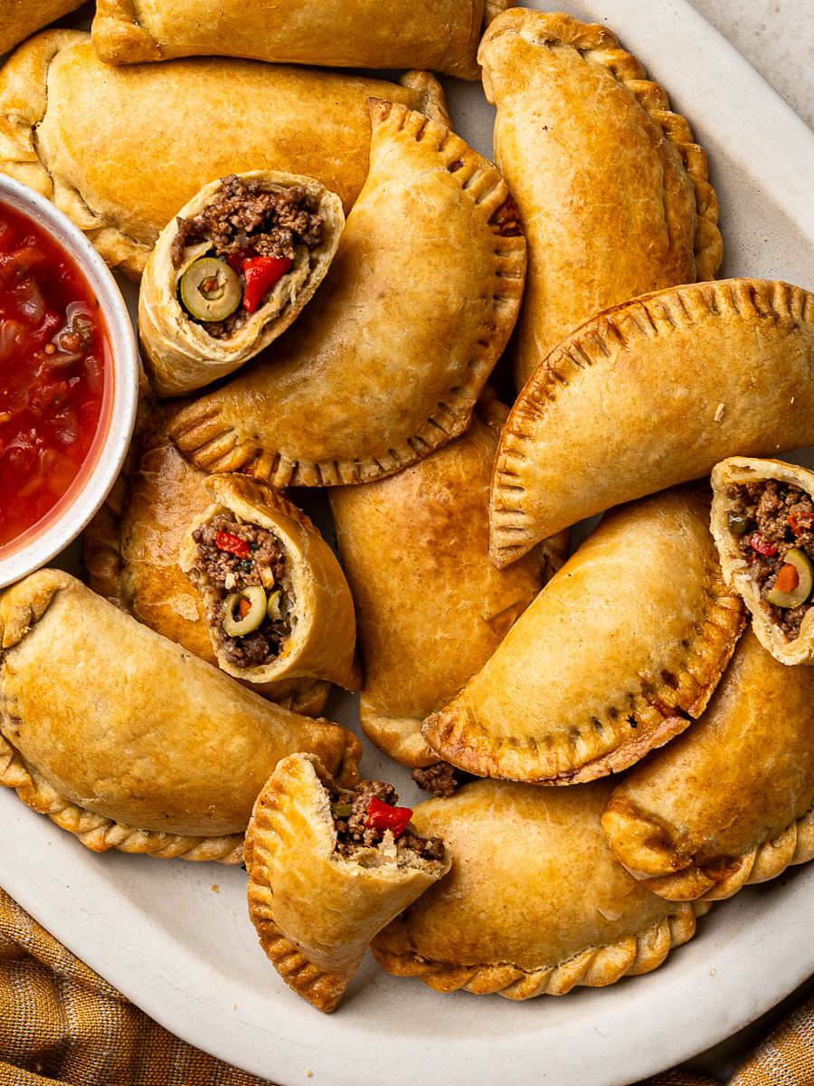Close up of baked beef empanadas with some broken to show filling.