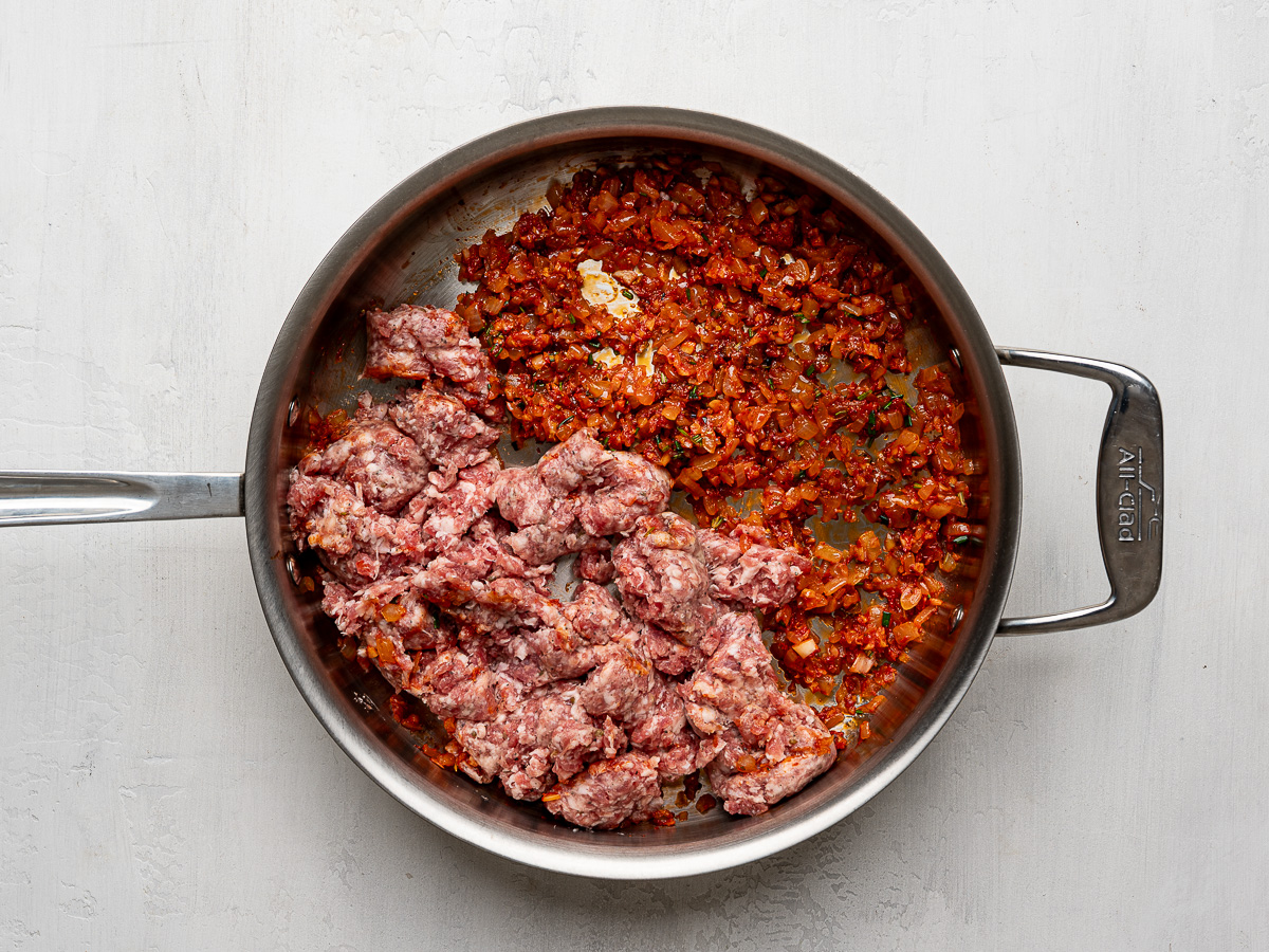 Adding raw sausage to onion mixture in stainless steel skillet.