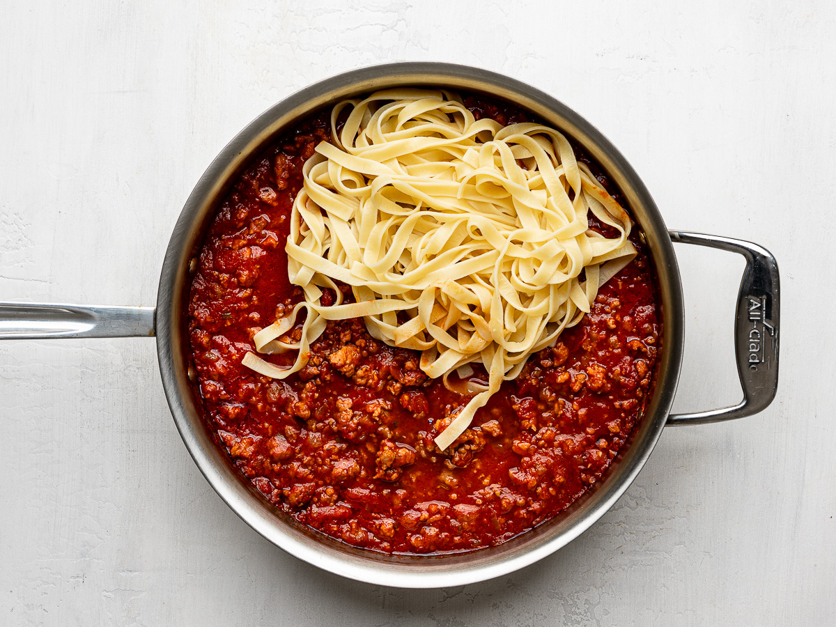 Adding cooked fettuccini noodles to sausage ragù in skillet.