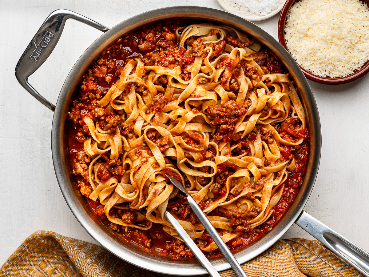 Pasta and sausage ragù mixed in large skillet with a bowl of parmesan cheese on the side.