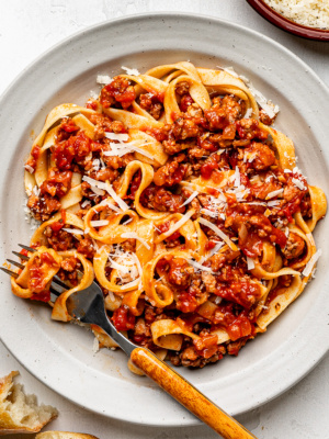 Close-up of fettuccini pasta and sausage ragù served on a beige shallow bowl.