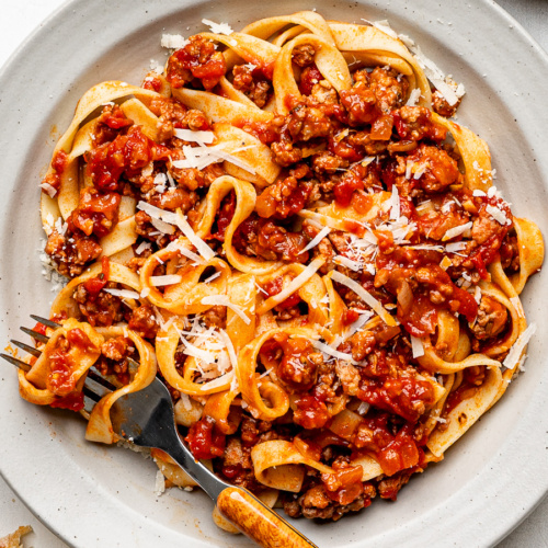 Close-up of fettuccini pasta and sausage ragù served on a beige shallow bowl.