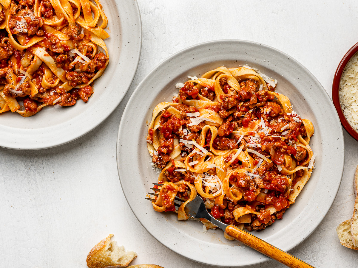 Fettuccini pasta and sausage ragù served on two beige shallow bowls.