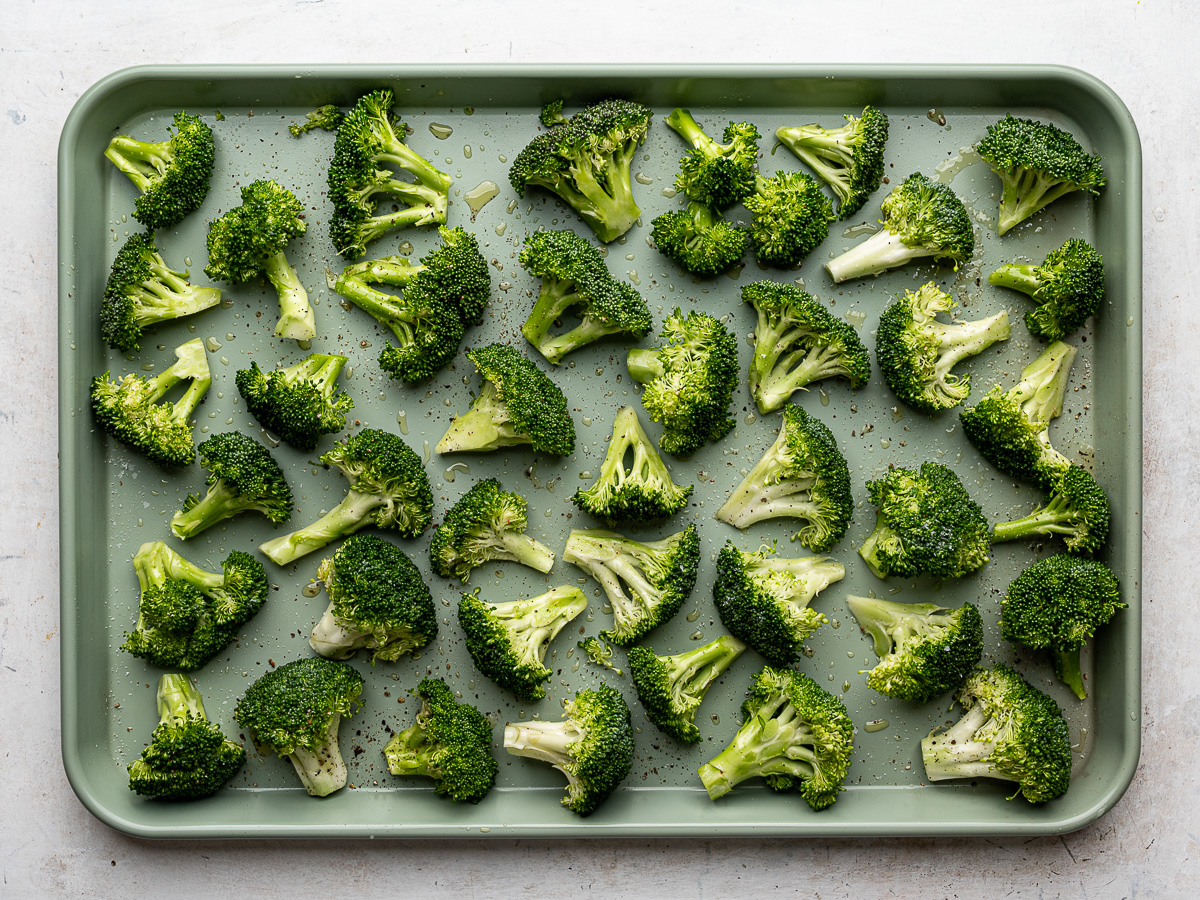 Raw broccoli florets tossed with olive oil, spread out evenly on a sheet pan.