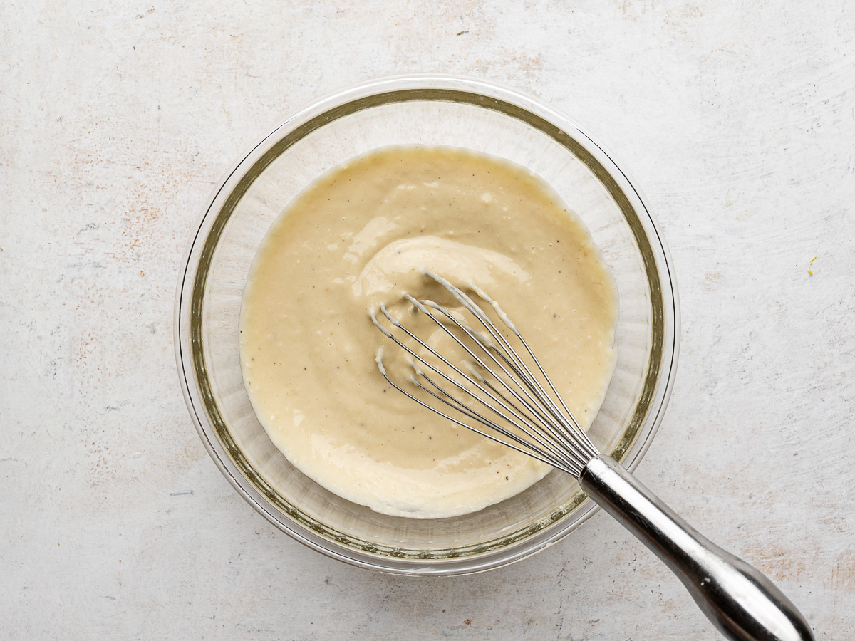 Caesar dressing combined in a bowl with whisk.