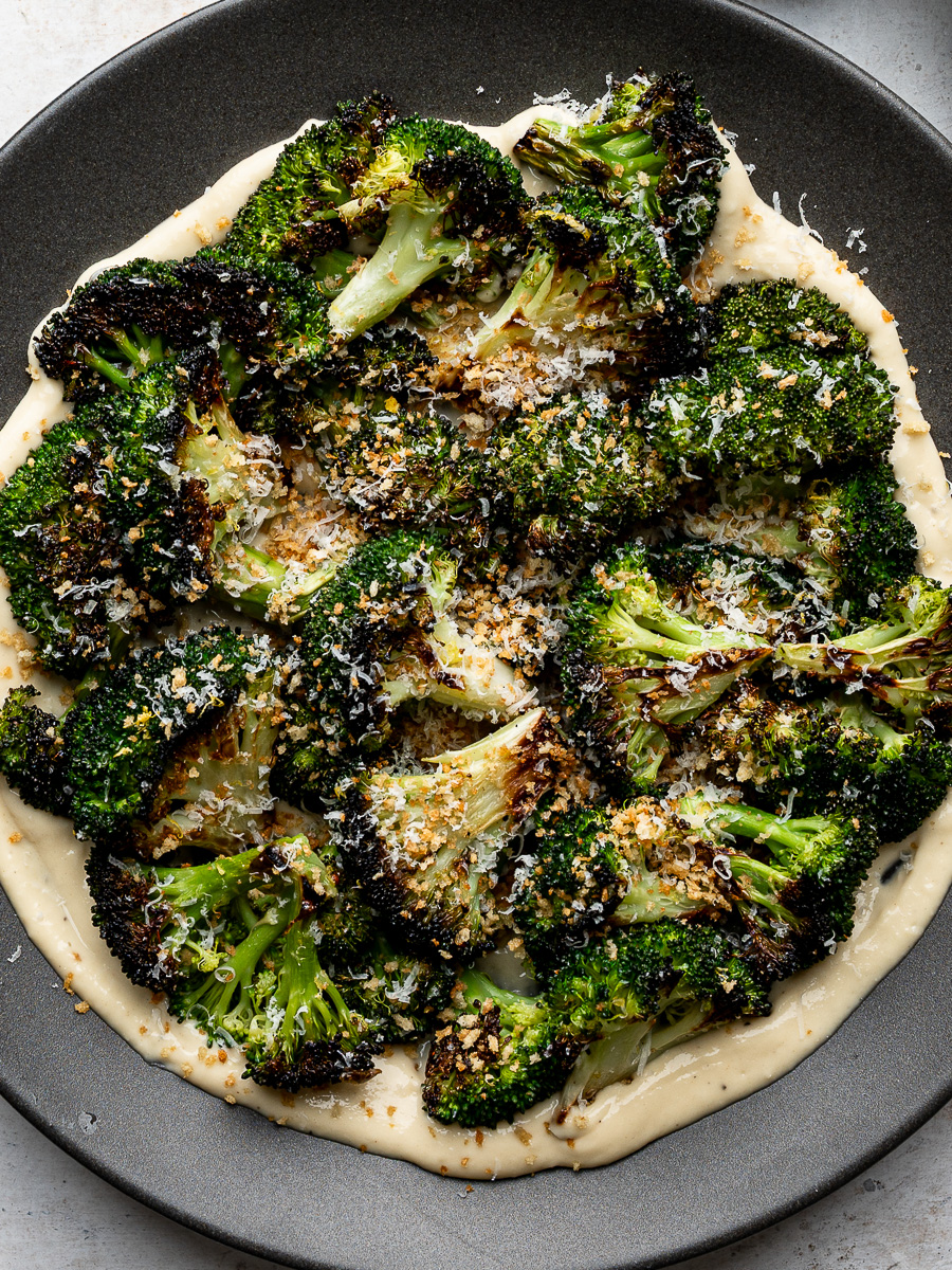 Close up of plated roasted broccoli florets arranged over a layer of Caesar dressing, sprinkled with toasted breadcrumbs and freshly grated Parmesan.