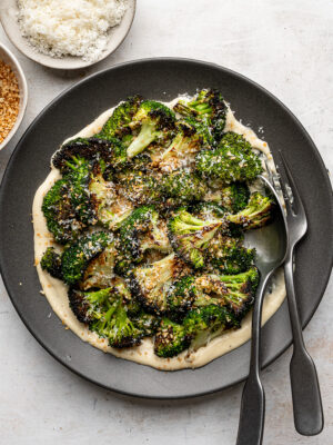 Plated roasted broccoli florets arranged over a layer of Caesar dressing, sprinkled with toasted breadcrumbs and freshly grated Parmesan.