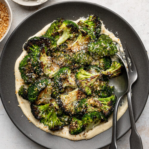 Plated roasted broccoli florets arranged over a layer of Caesar dressing, sprinkled with toasted breadcrumbs and freshly grated Parmesan.