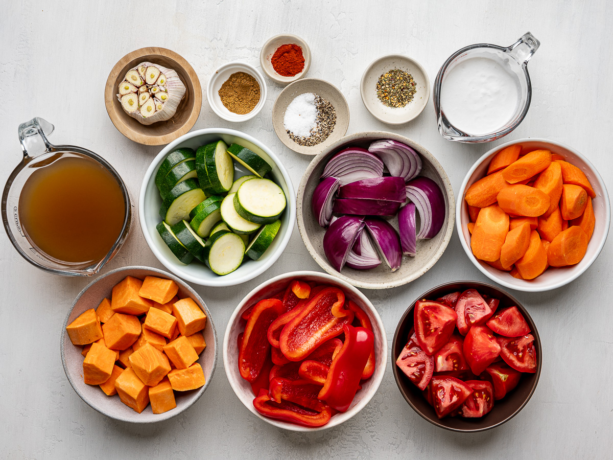 Individual bowls of chopped vegetables for sheet pan soup, including carrots, zucchini, red peppers, and tomatoes.