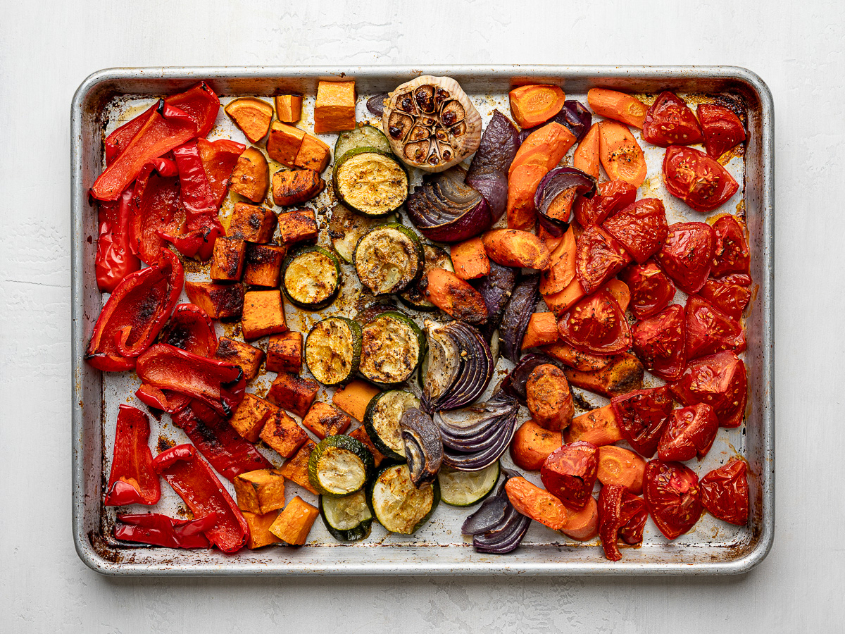 Caramelized roasted vegetables including carrots, peppers, zucchini, and sweet potatoes on a sheet pan.