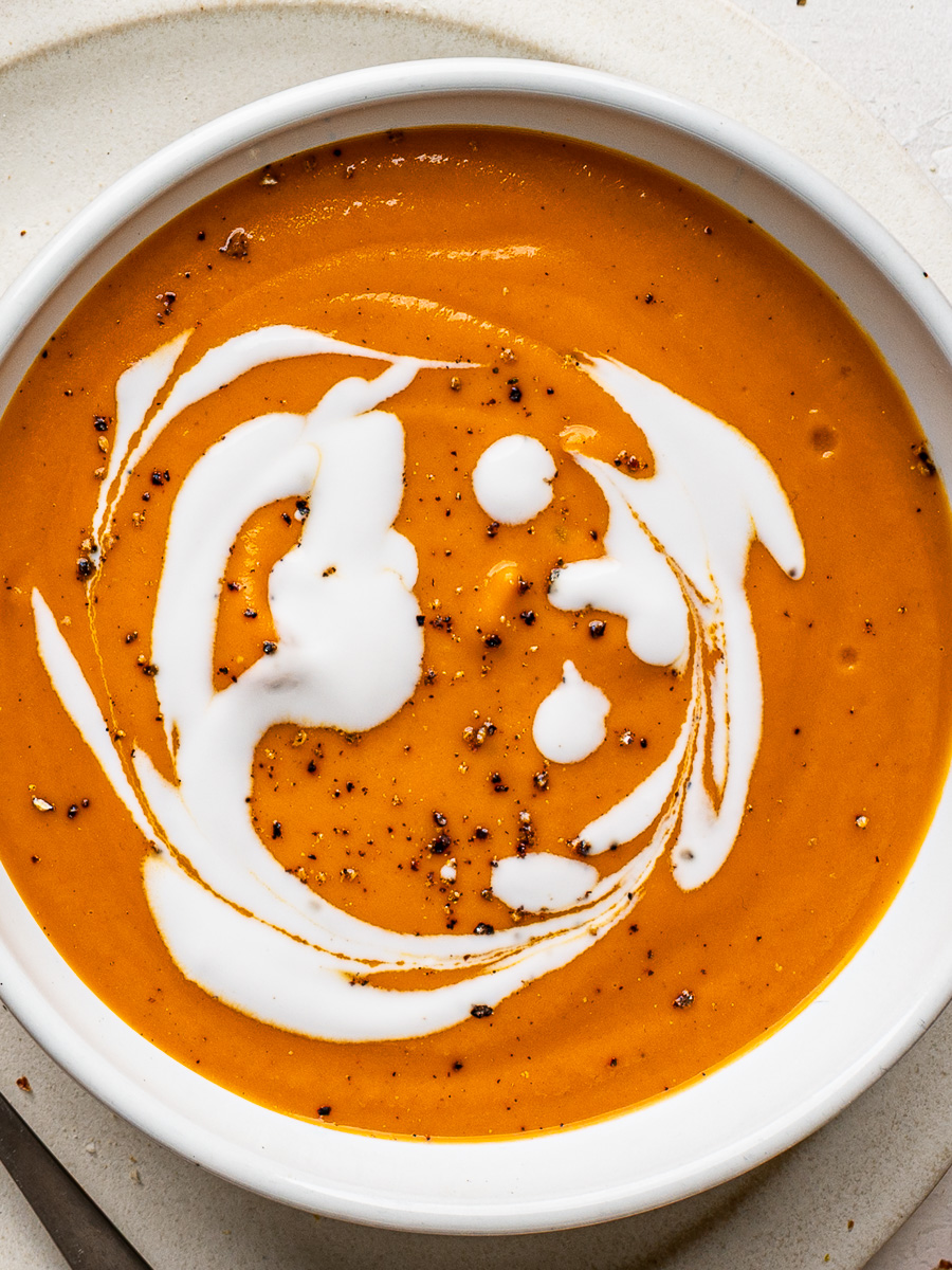 Close-up of creamy sheet pan vegetable soup in a white bowl, garnished with a swirl of coconut milk and ready to enjoy.