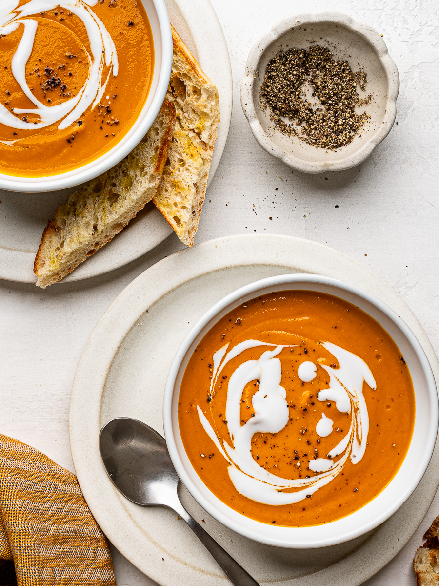 Two bowls of creamy sheet pan vegetable soup, garnished with a swirl of coconut milk and ready to enjoy.
