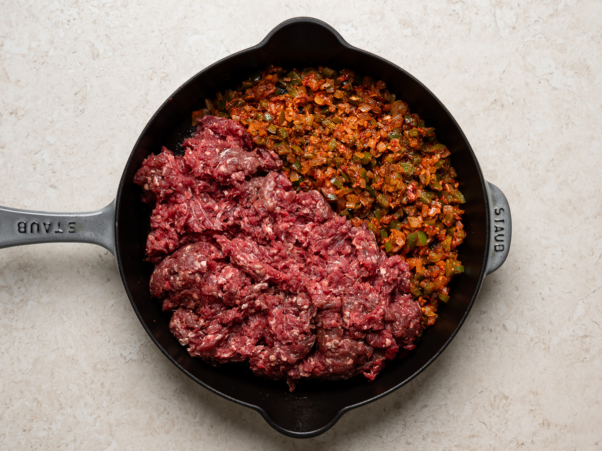adding raw beef to skillet with sautéed aromatics.