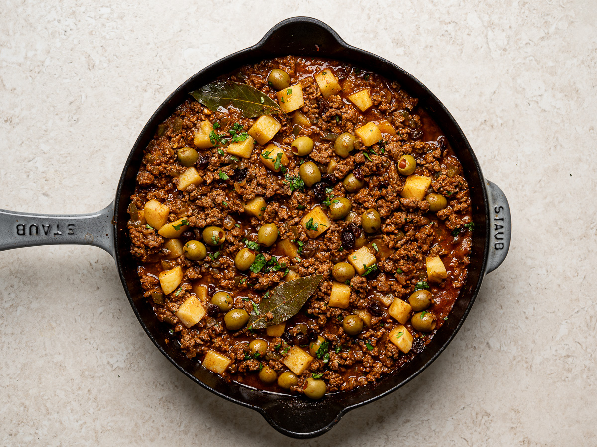 Cooked beef picadillo with cubed potatoes in skillet.