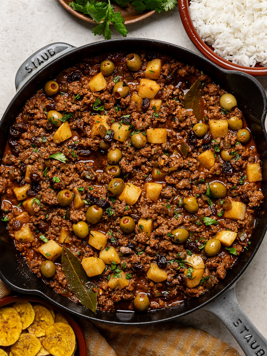 Picadillo in skillet with white rice and plantain chips on the side.