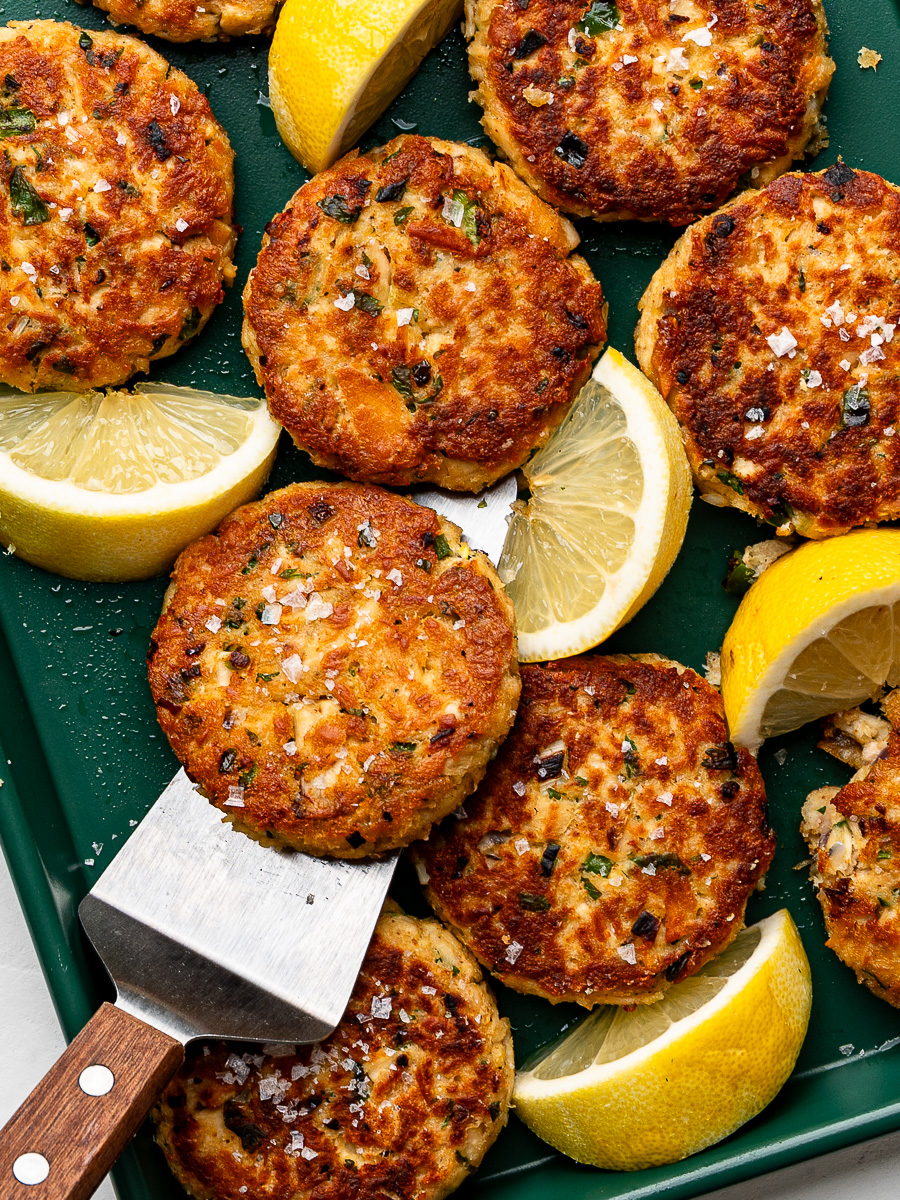 Pan-fried tuna patties on green baking sheet with lemon wedges.