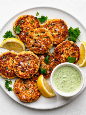 Pan-fried tuna patties on white plate with lemon wedges and dipping sauce on the side.