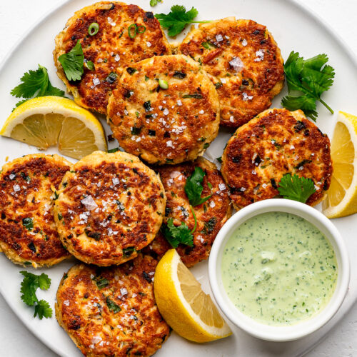 Pan-fried tuna patties on white plate with lemon wedges and dipping sauce on the side.