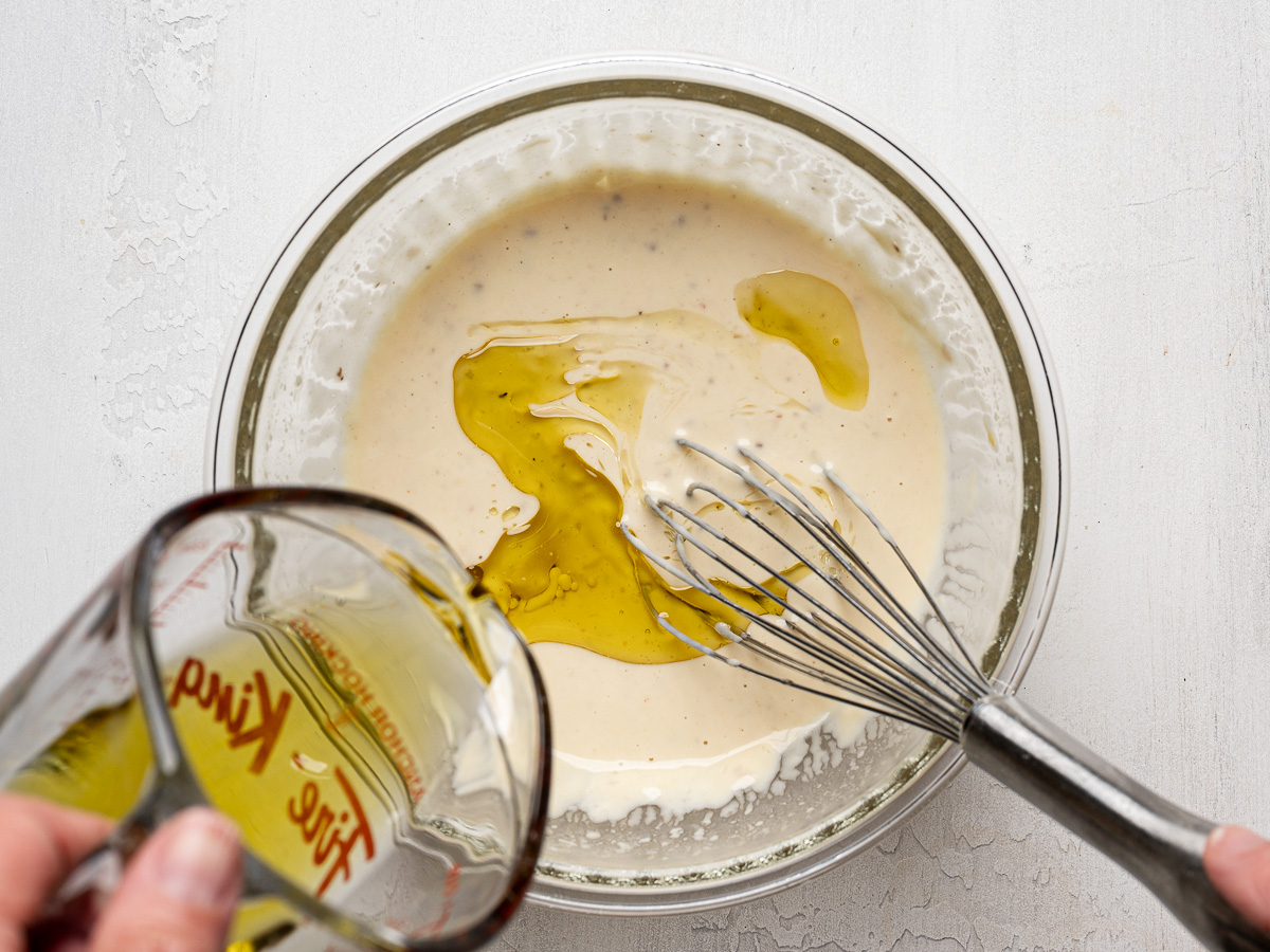 Slowly drizzling olive oil into dressing.