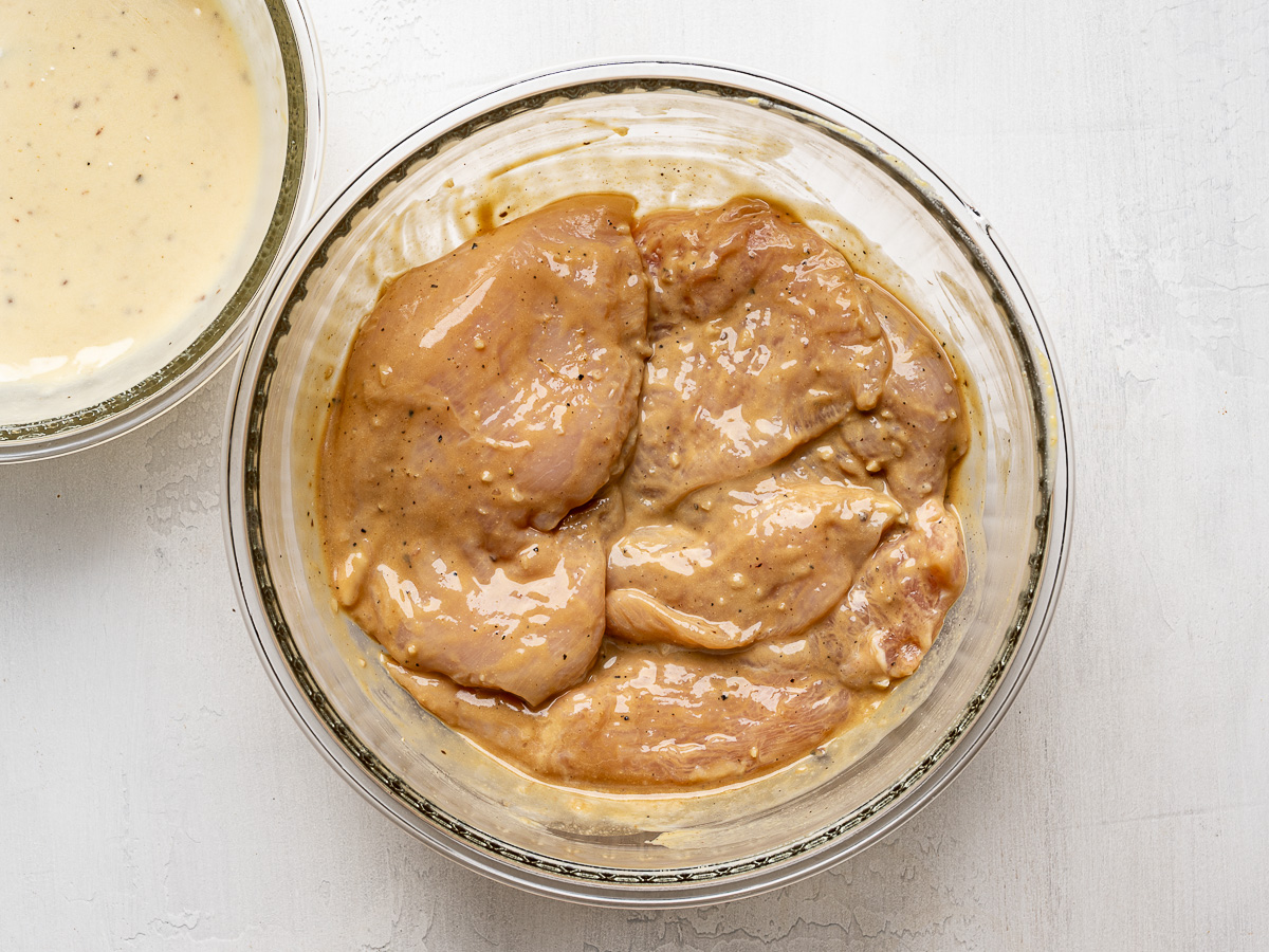 Chicken marinating in a bowl with Caesar Dressing.
