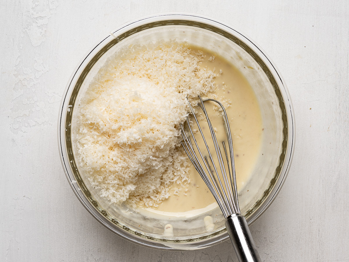 Grated parmesan cheese added to Caesar Dressing in bowl.