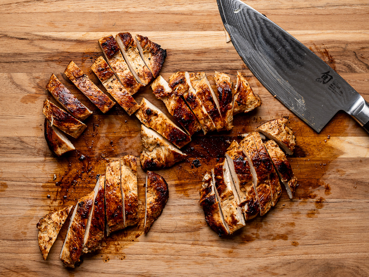 Chicken breasts slices into strip on wood cutting board.