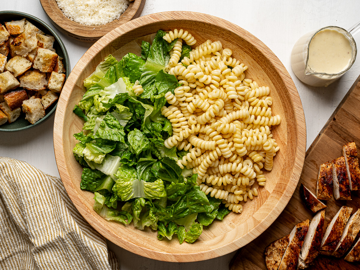 Romaine lettuce and cooked pasta in a wooden salad bowl.