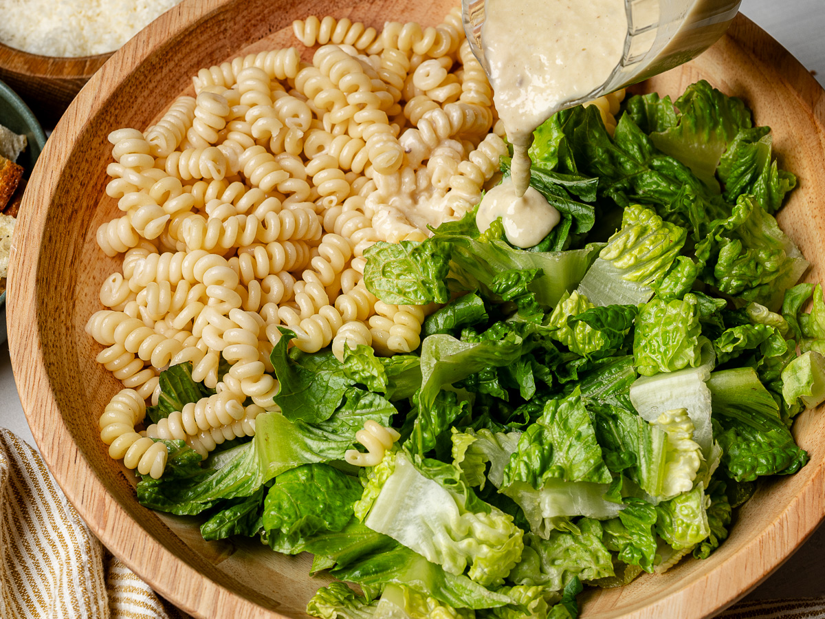 Close-up of drizzling dressing over lettuce and pasta.