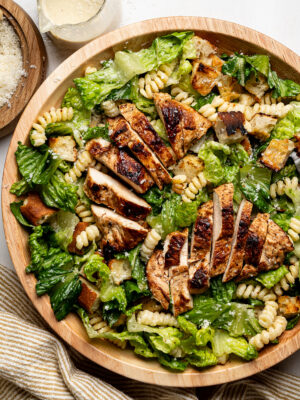 Caesar Pasta Salad in a large wood bowl with pan-fried chicken slices on top.
