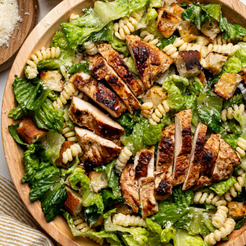 Caesar Pasta Salad in a large wood bowl with pan-fried chicken slices on top.