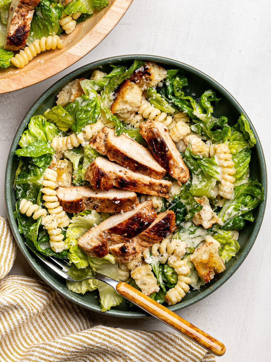 Chicken Caesar pasta salad served in a green bowl topped with chicken slices.