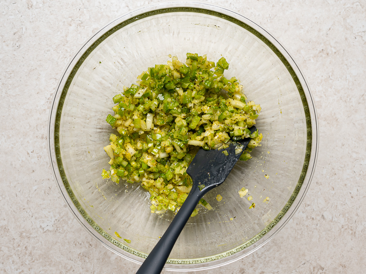 Celery-onion mixture combined in mixing bowl with spatula.