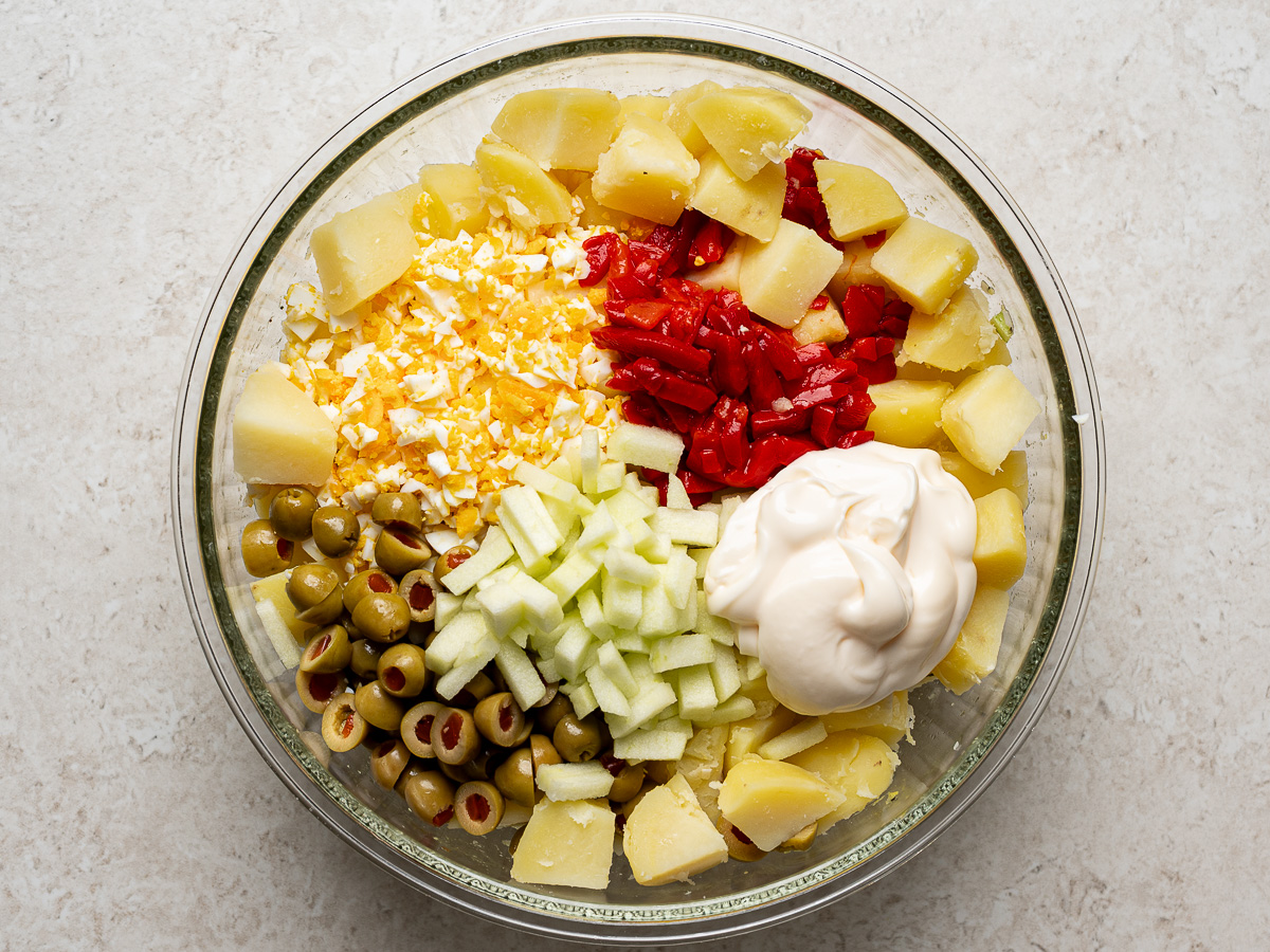 Adding rest of ingredients—mayo, eggs, olives and pimientos—to cooled potatoes.