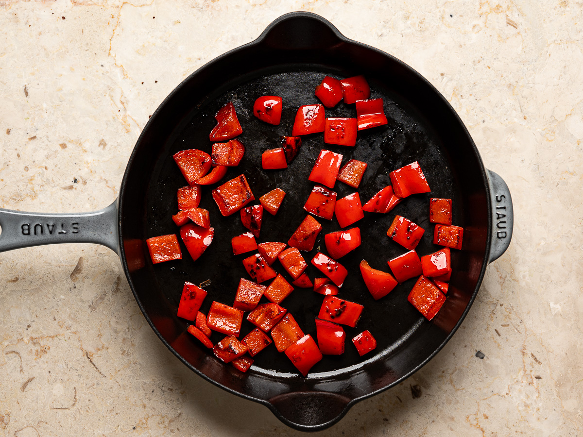 Diced red bell peppers sautéed in skillet.