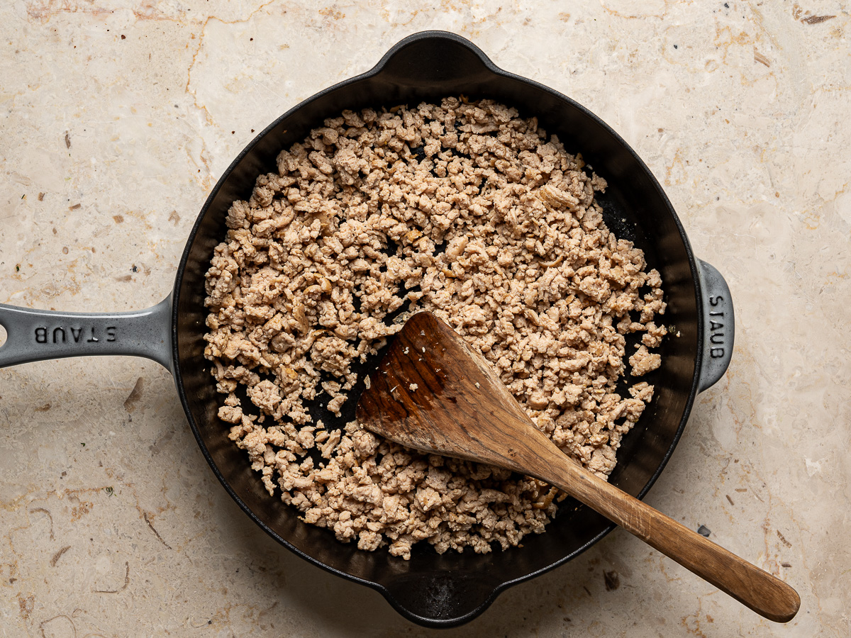 Cooked and browned ground chicken in skillet with wooden spoon.