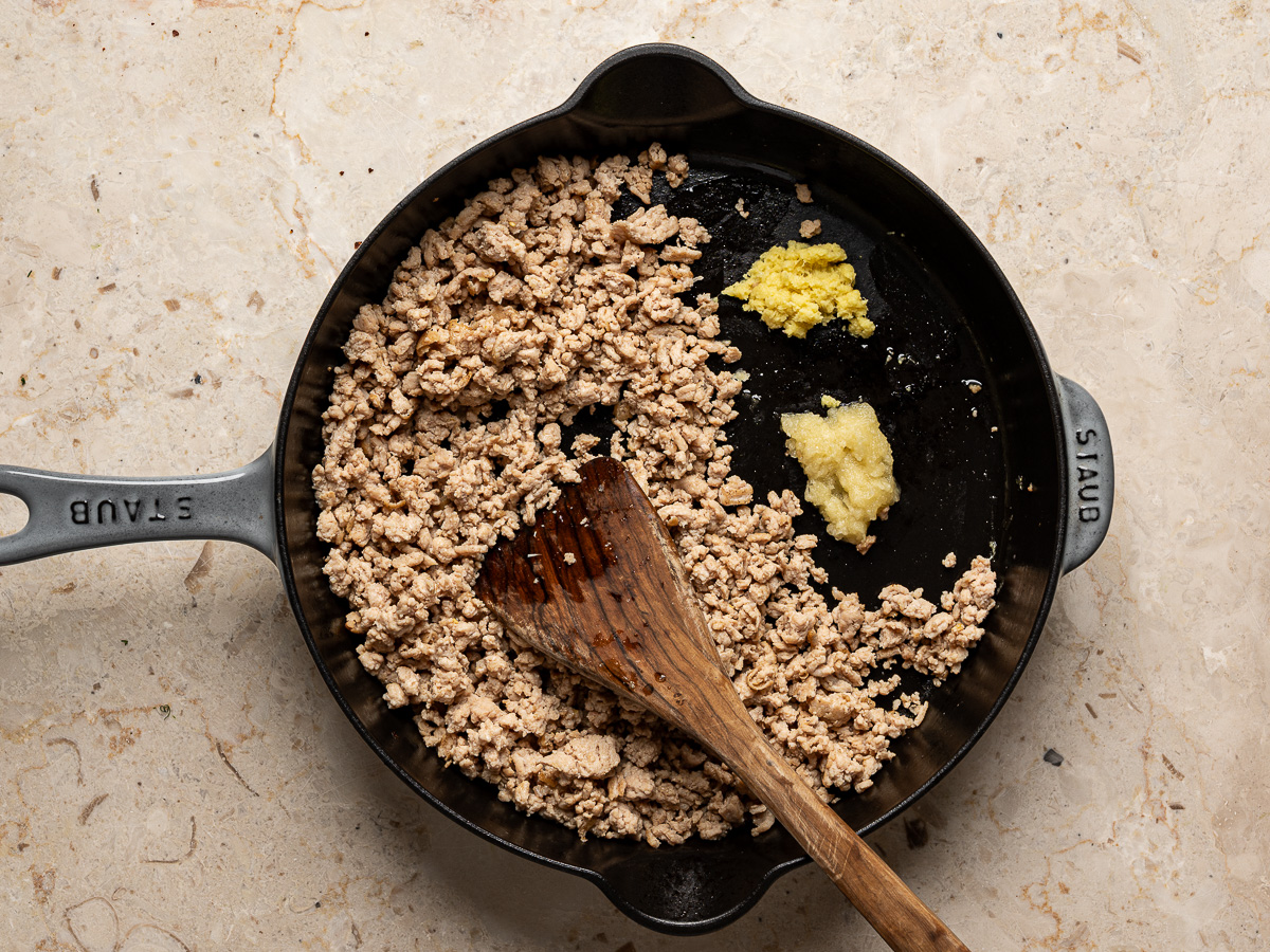 Grated ginger and garlic added to ground chicken in skillet.